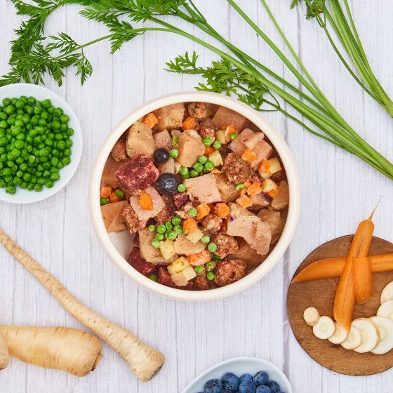BARF Gourmet PLUS Huhn mit Fleischstücken und Gemüse in Schale, umgeben von frischen Zutaten.
