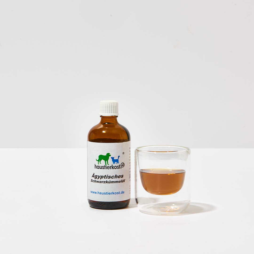 Flasche ägyptisches Schwarzkümmelöl 100 ml neben Glas mit Öl für Fell- und Hautpflege bei Tieren, nicht für Katzen geeignet