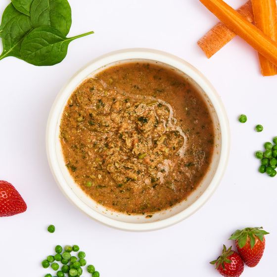 Pürierter Obst- und Gemüse-Mix mit Karotten, Erbsen, Spinat und Erdbeeren in einer Schüssel, umgeben von frischen Zutaten.