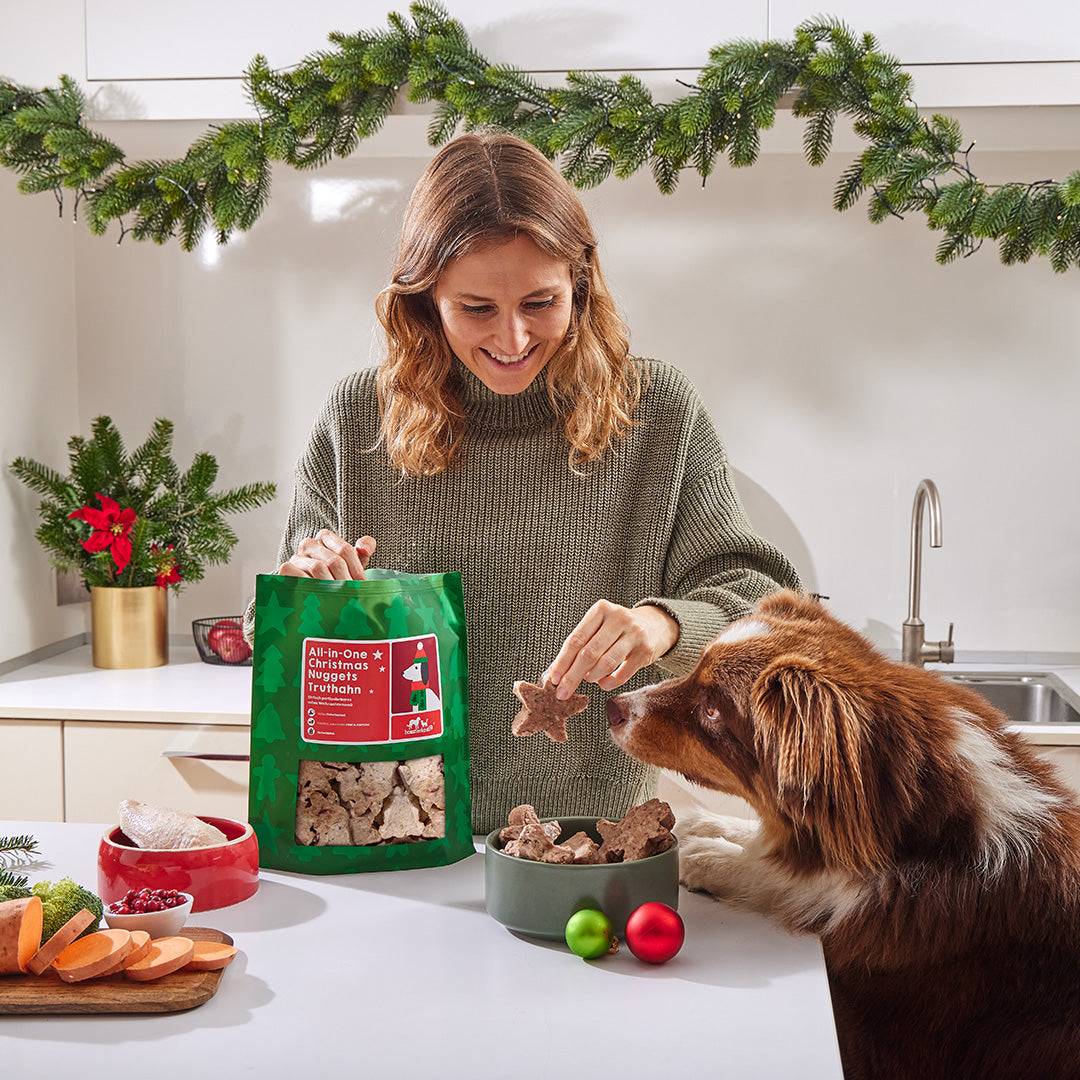 Frau serviert festliches Komplettmenü mit Truthahn, Süßkartoffeln und Cranberries, BARF-geeignet. Hund wartet gespannt.